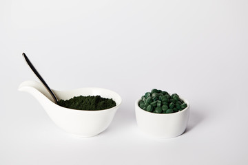 spoon, spirulina powder and spirulina pills in bowls on grey background