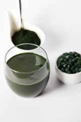 close up view of fresh spirulina drink in glass, spirulina powder and spirulina pills in bowls on grey background