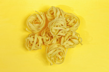 Close up of a raw dry italian pasta fettuccine on bright yellow background. Shooting with bold color.