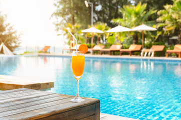 Fototapeta na wymiar Orange juice glass on wooden table with swimming pool view background