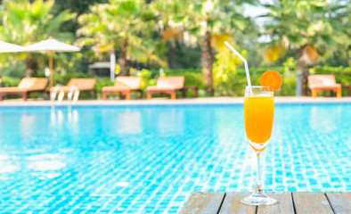 Orange juice glass on wooden table with swimming pool view background