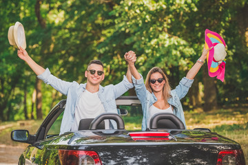 Happy fashionable couple with arm raised in convertible car freedom concept.