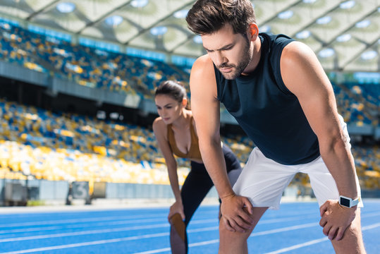 young tired couple standing on running track at sports stadium after jogging