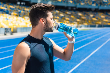 Fototapeta na wymiar attractive young man drinking water after training at sports stadium