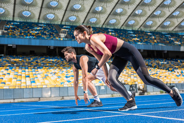 athletic young male and female sprinters in start position on running track at sports stadium