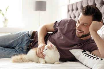 Young man with cute cat on bed at home
