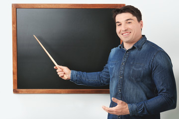 Portrait of male teacher with pointer near chalkboard in classroom
