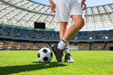 cropped shot of soccer player standing with ball at sports stadium
