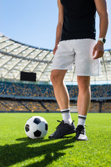 cropped shot of soccer player standing with ball at modern sports stadium