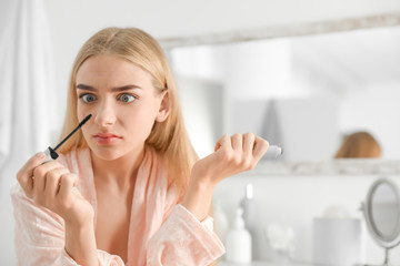 Emotional woman holding mascara brush with fallen eyelashes indoors
