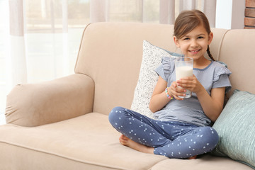 Cute little girl with glass of milk on sofa at home