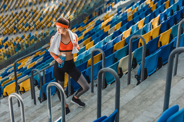 Obraz premium high angle view of beautiful young woman with water bottle and towel at sports stadium