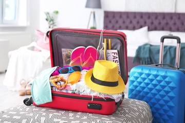 Open suitcase with different clothes and accessories for summer journey on ottoman chair