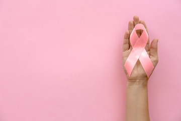 Woman holding symbolic ribbon of breast cancer awareness on color background, top view. Gynecological care