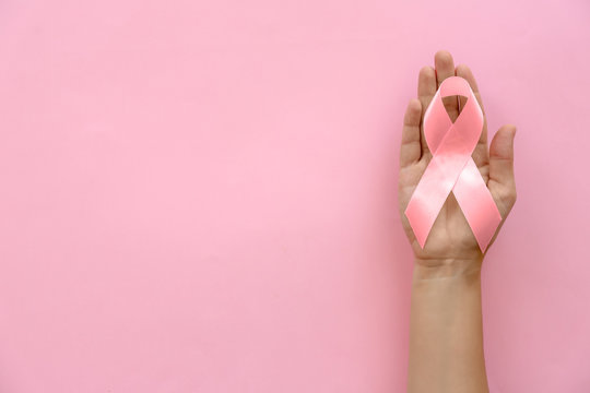 Woman holding symbolic ribbon of breast cancer awareness on color background, top view. Gynecological care