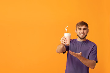 Young man with glass of delicious milk shake on color background