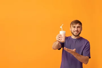 Papier Peint photo Milk-shake Young man with glass of delicious milk shake on color background