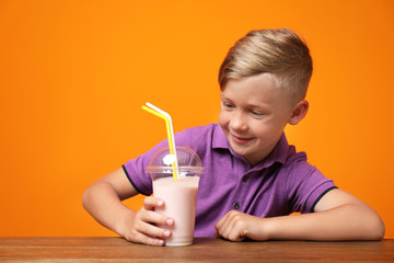 Little boy with cup of milk shake at table on color background