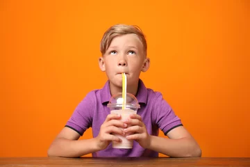 Photo sur Plexiglas Milk-shake Petit garçon avec une tasse de milk-shake à table sur un fond de couleur