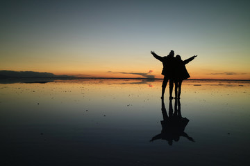 Silhouette of a couple raising their arms for the happy moment on the incredible mirror effect of Uyuni Salt Flats, Bolivia, South America 