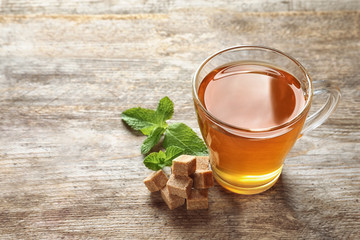 Cup with hot aromatic mint tea, fresh leaves and sugar cubes on wooden table