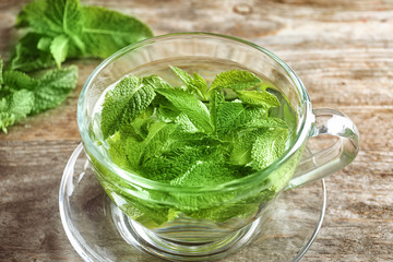 Cup with hot aromatic mint tea on wooden table