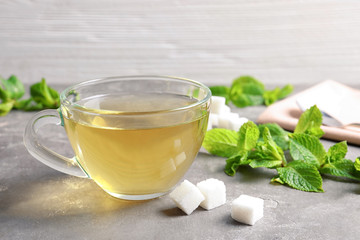 Cup with hot aromatic mint tea, fresh leaves and sugar cubes on table