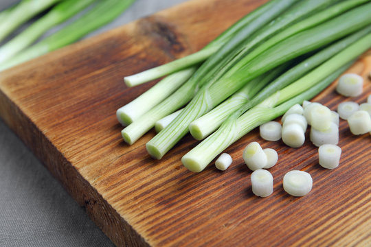 Wooden board with fresh green onion, closeup