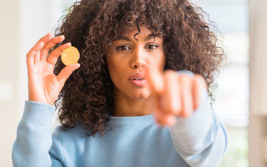 African american woman holding golden bitcoin cryptocurrency at home pointing with finger to the camera and to you, hand sign, positive and confident gesture from the front