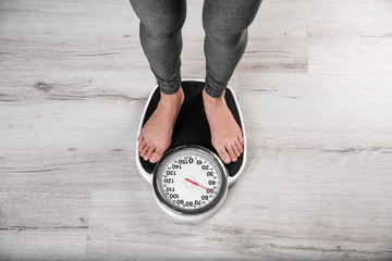 Young woman measuring her weight using scales on floor, top view. Weight loss motivation