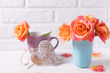 Fresh  bright roses in blue cup and decorative heart  on white wooden background against white wall.