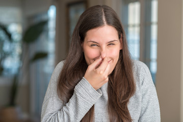 Fototapeta premium Young beautiful woman at home smelling something stinky and disgusting, intolerable smell, holding breath with fingers on nose. Bad smells concept.