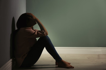 Depressed young woman sitting on floor in darkness