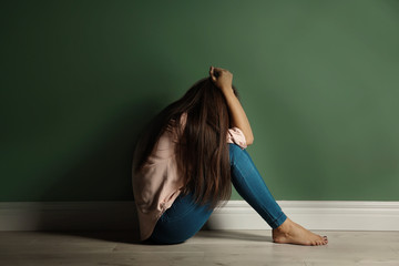 Fototapeta na wymiar Depressed young woman on floor near color wall