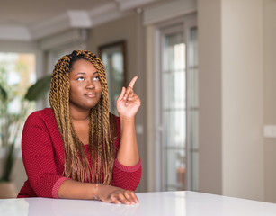 African american woman sitting at home surprised with an idea or question pointing finger with happy face, number one