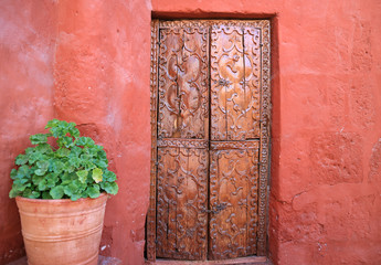 Old carved wood door on the orange red color rough wall with a big terracotta planters in Santa Catalina Monastery, Arequipa of Peru