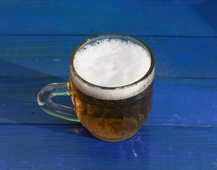 A small mug of beer on a blue wooden background.