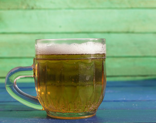 A small mug of beer on a blue wooden background.