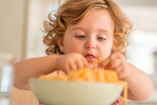 Close up of beautiful blond child eating spaghetti with hands at home.