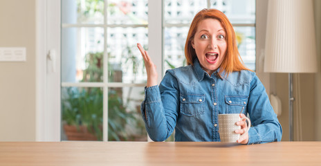 Redhead woman holding a cup of coffee very happy and excited, winner expression celebrating victory screaming with big smile and raised hands