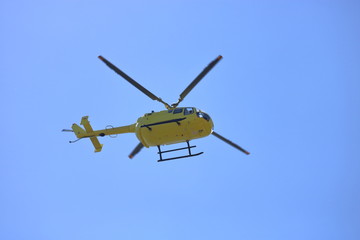 Żółty helikopter w powietrzu w trakcie lotu, widok z dołu, z ziemi