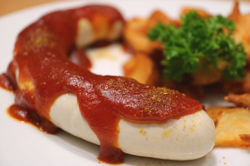 Close-up of German style white sausage with curry tomato sauce with blurred fried potatoes in background 