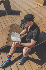 a student in a shirt and glasses reading a book in the city Park