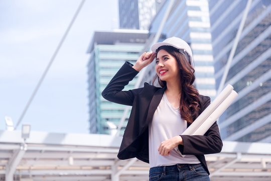 Portrait of Happy professional construction engineer woman holding the blueprint and wearing the safety helmet and glasses at the building site place background,