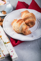 Close up shot of croissants on white plate next to cup of coffee with marshmallow and sweets . With space for text.