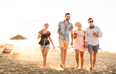 Group of happy friends having fun at seaside sunset - Summer vacations and friendship concept with young people millennials walking at beach - Warm sunshine filtered color tone with focus on left girl