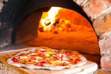 Rustic home-made pizza prosciutto baked in a wood fired brick oven with fire burning in the...