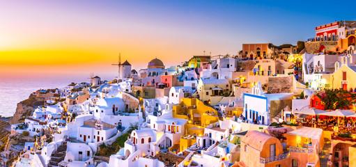 Panoramic view of Oia town, Santorini island, Greece at sunset. Traditional and famous white houses and churches  with blue domes over the Caldera, Aegean sea. - obrazy, fototapety, plakaty
