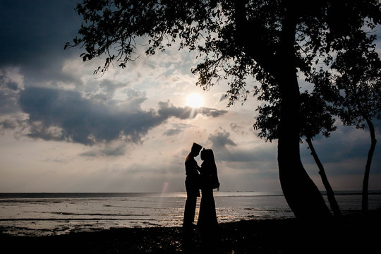 young couple on their wedding day going outdoor at the beach during sunset to take silhouette picture 