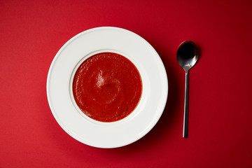 elevated view of tomato soup in plate and spoon on red table